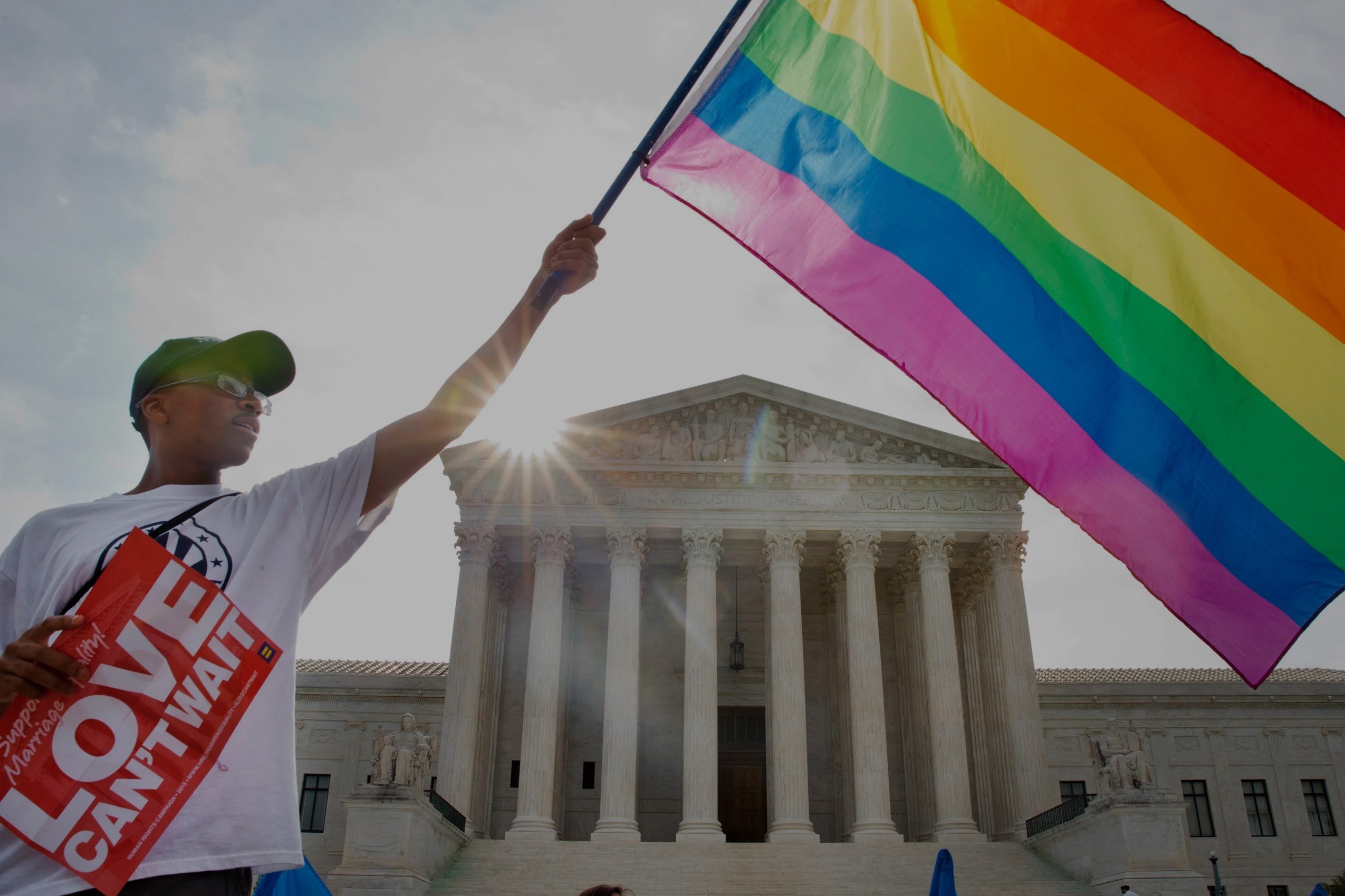 An image of a person holding a pride flag in front of the White House.